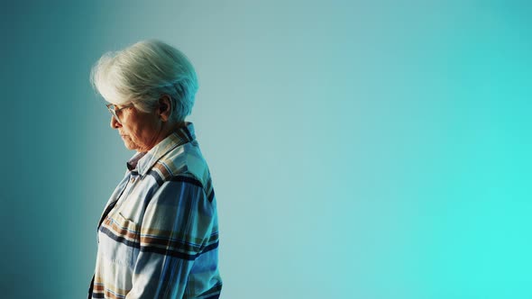 Elderly Woman Sad Looking to the Light Source Over Blue Studio Background