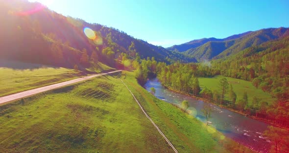 Mid Air Flight Over Fresh Mountain River and Meadow at Sunny Summer Morning. Rural Dirt Road Below