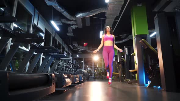 Full-length of a sportive woman in pink top and leggings jumping on rope in fitness center.