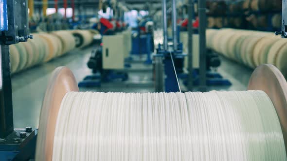 White Wire Unwinding From a Large Wooden Spool at a Factory