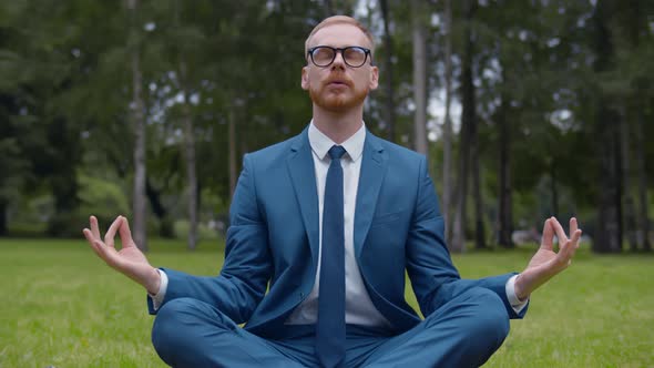 Relaxed Businessman Sitting on Lawn Doing Meditation in City Park