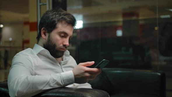 Young Male Checks Social Networks on a Mobile Phone While Waiting for a Haircut
