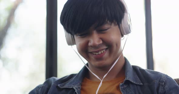 Happy young Asian man listening for music with headphone in living room.