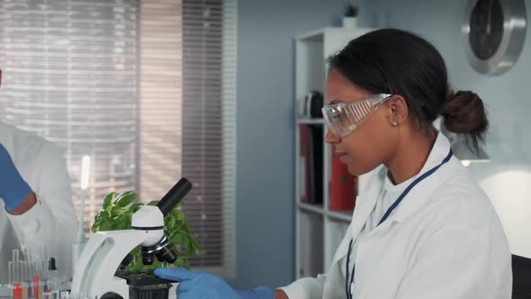 Mixed Race Woman in Lab Coat and Safety Glasses Working with Microscope
