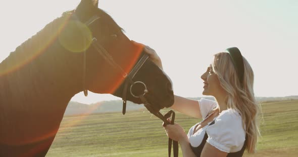 Girl in Has a Fun and Caresses a Brown Horse Among Wide Meadows with Sun Beams