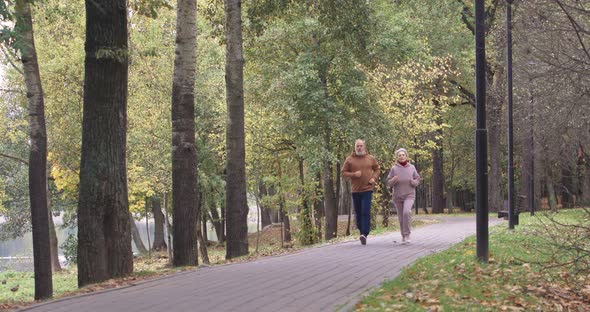 Wellness, Adult Couple Running Around a Forest Park, Autumn Day, Gray-haired Man and a Woman Plays