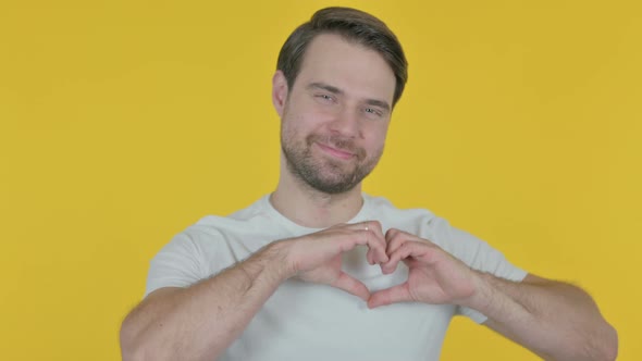 Young Man showing Heart Shape by Hands on Yellow Background