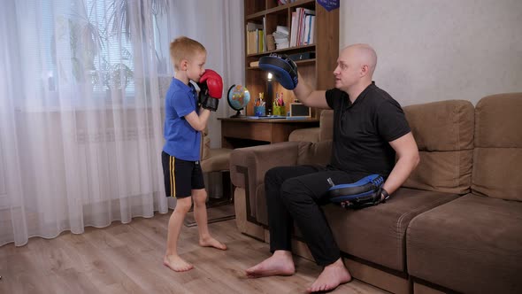 A Boy in Boxing Gloves Trains at Home with His Father