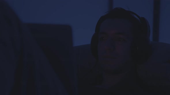 Young Man in Headphones Watching Film Movie on Laptop While Resting on Bed at Night
