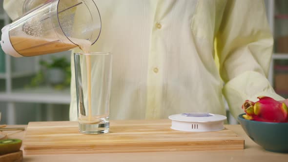 Young Woman Pouring Smoothie Into Glass From Blender Closeup Cooking Sweet Detox Juice in Kitchen