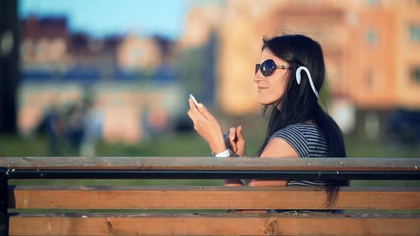Young Brunette Straight Hair Woman in the Park Listening to Music with Headphones and Smartphone