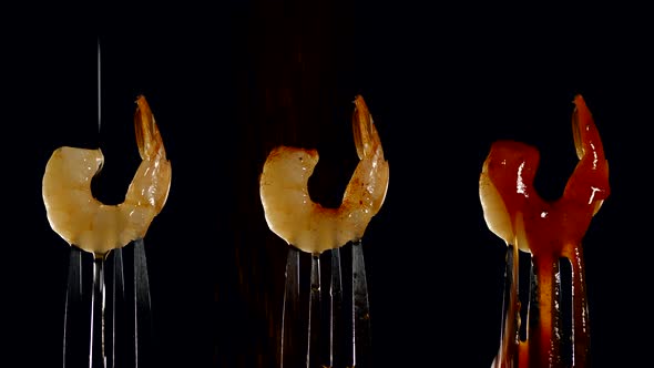 freshly cooked juicy shrimp on a fork is poured with oil, seasoning and sauce on a black background.