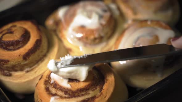 Close up knife spreading sweet icing on warm homemade cinnamon buns