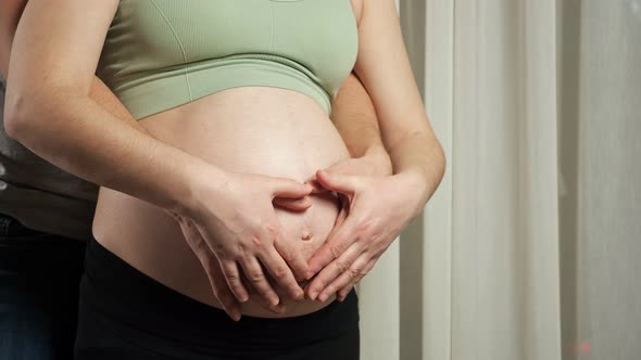 Husband and Wife Make Heart Sign Hugging Pregnant Belly