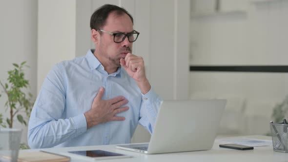 Middle Aged Man Coughing While Using Laptop in Office