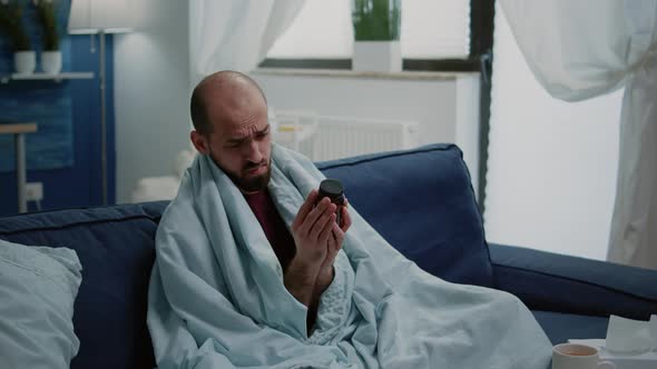 Sick Man Reading Label of Bottle with Pills and Drugs