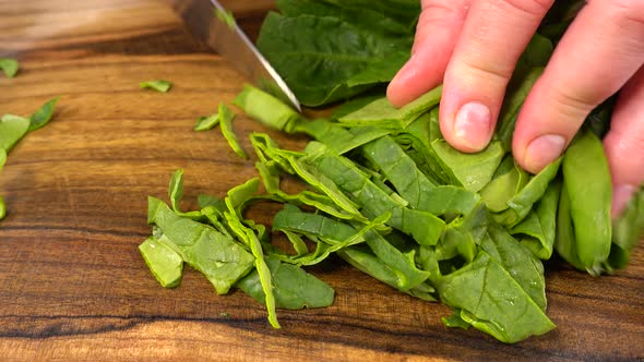 The cook cuts spinach leaves on a wooden cutting board.