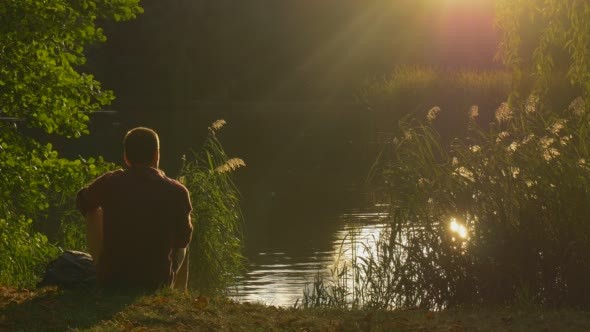 Man With Backpack Comes Sits at The Lake Bank