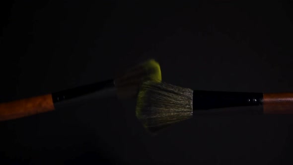 slow motion of two make up brushes with yellow powder explosion and burst on black background