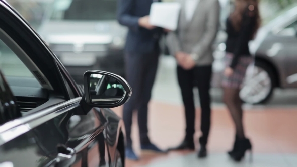 Blurred Couple And Seller Behind a Car alt