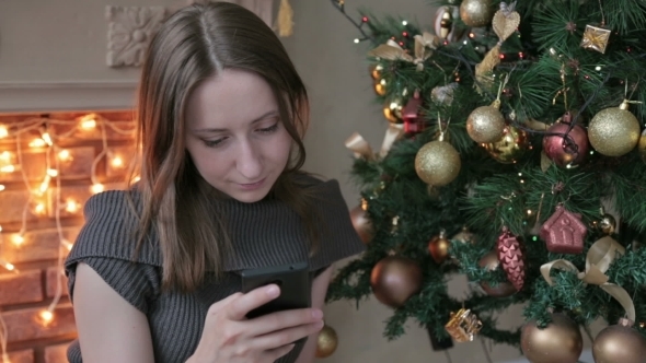 Woman Using Her Mobile Phone At Christmas At Home