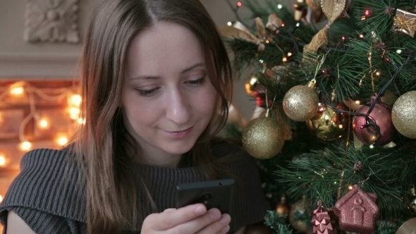 Woman Using Her Mobile Phone At Christmas At Home