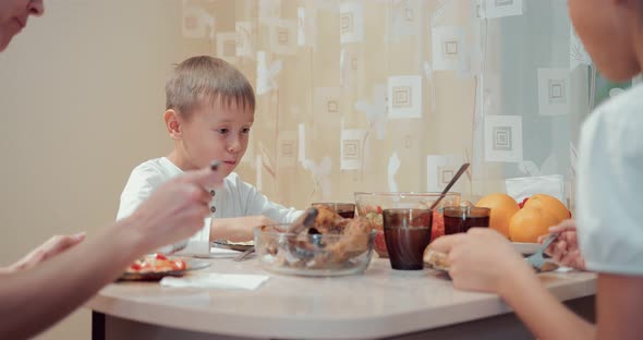 Small and Beautiful Son is Having Dinner with His Family in the Kitchen