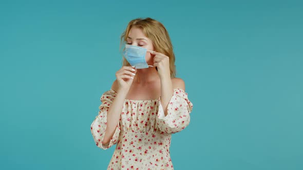 Young Pretty Girl Puts on Face Medical Mask During Coronavirus Pandemic. Portrait on Blue Background