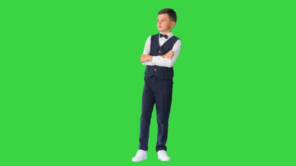 Little Boy in a Bow Tie Standing with Crossed Arms and Looking Up on a Green Screen Chroma Key