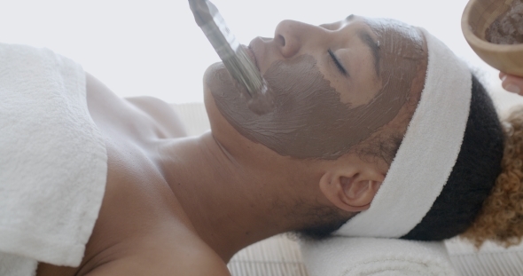 Woman With Clay Facial Mask In Spa