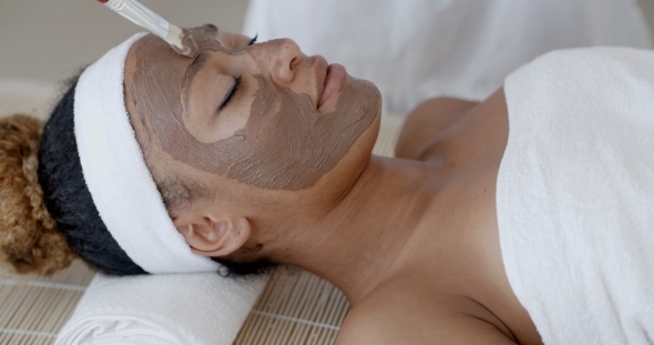 Woman With Clay Facial Mask In Spa