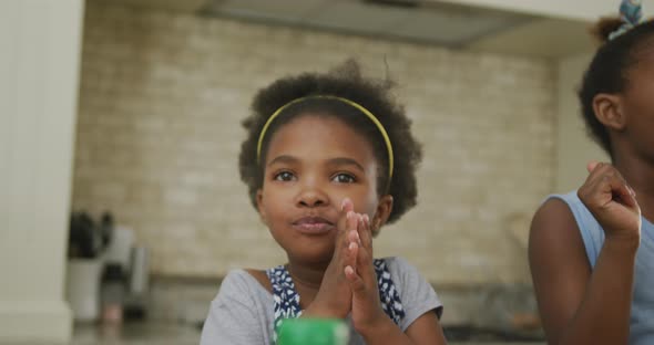 Happy african american girls eating and waving hands in kitchen