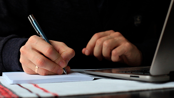 Man Working On Laptop And Writing In a Notebook