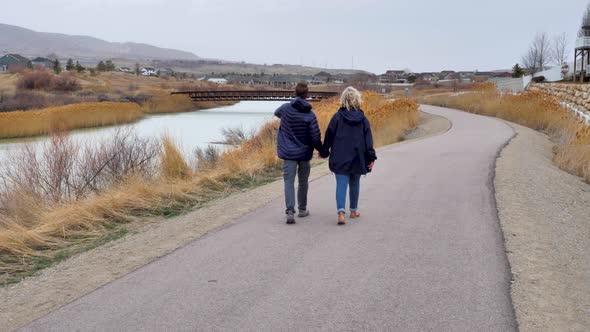 A young couple walking along a neighborhood nature trail hand in hand on a overcast afteroon - rear