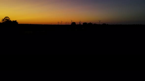 Wind turbines producing green energy. Windmill silhouettes in sunset. Aerial