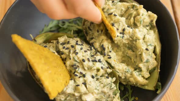 Person Dips Yellow Crisp Into Dessert in Avocado Peel Close