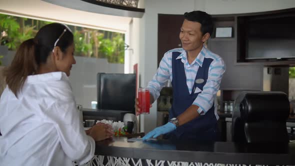 Young Asian Lady in White Shirt Sitting at Bar Counter of Open Cafe, Bartender Serving a Red Drink