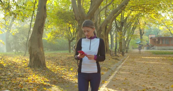 Portrait of Young Woman After Running and Using Smart Phone on the City Park Background