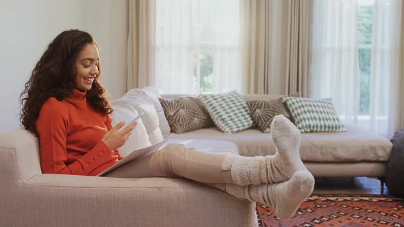 Happy woman sitting on sofa using her mobile phone