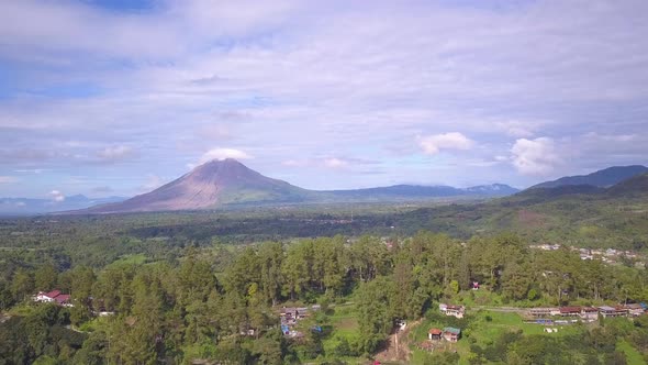 Aerial footage flying over a beautiful green village towards mount Sinabung volcano. Berastagi, Indo