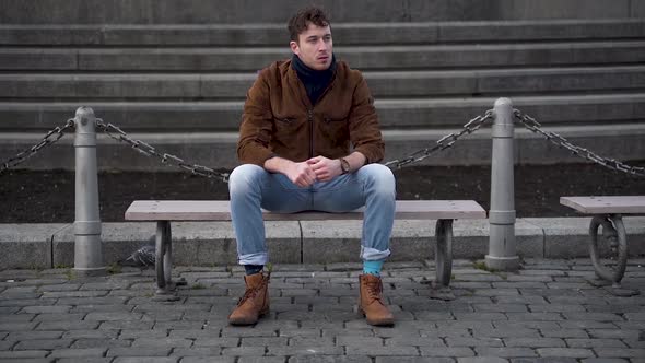 Young man waiting on a city bench,annoyed,checking his watch.