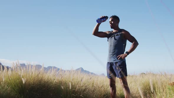 African american man exercising outdoors drinking water in countryside on a coast