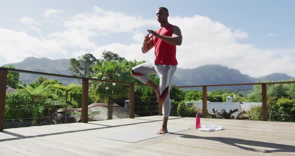 Focused biracial man practicing yoga on mat on terrace