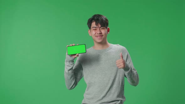 A Smiling Asian Man Holding Mobile Phone With Green Screen While Standing In Front Of Green Screen