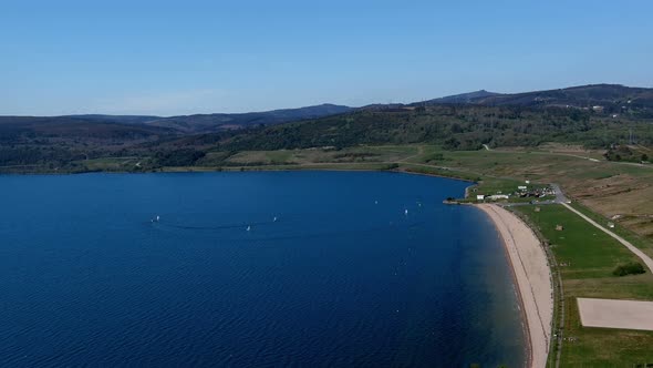 people enjoying the lake beach with gardens, sailboats sailing on a sunny afternoon. Drone shooting