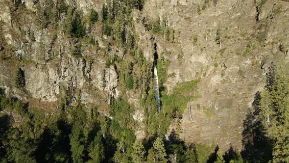 Aerial rising over Corbata Blanca thaw waterfall hiding between steep mountains with pine trees, Pat