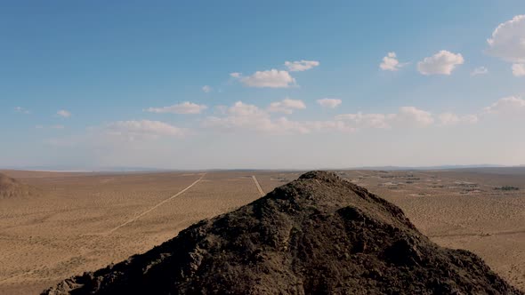 Rocky mountaintop in vast Mojave Desert plain landscape, Aerial Pull
