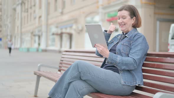 Old Woman Celebrating Online Win on Tablet While Sitting Outdoor on Bench