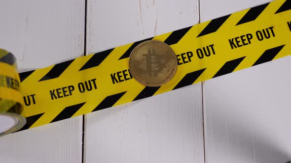 A Bitcoin Coin Lying on a Yellow Warning Tape with the Inscription KEEP OUT