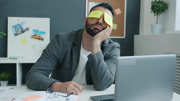 Inefficient Office Worker Sleeping at Desk in Workplace with Sticky Notes Showing Open Eyes on Face
